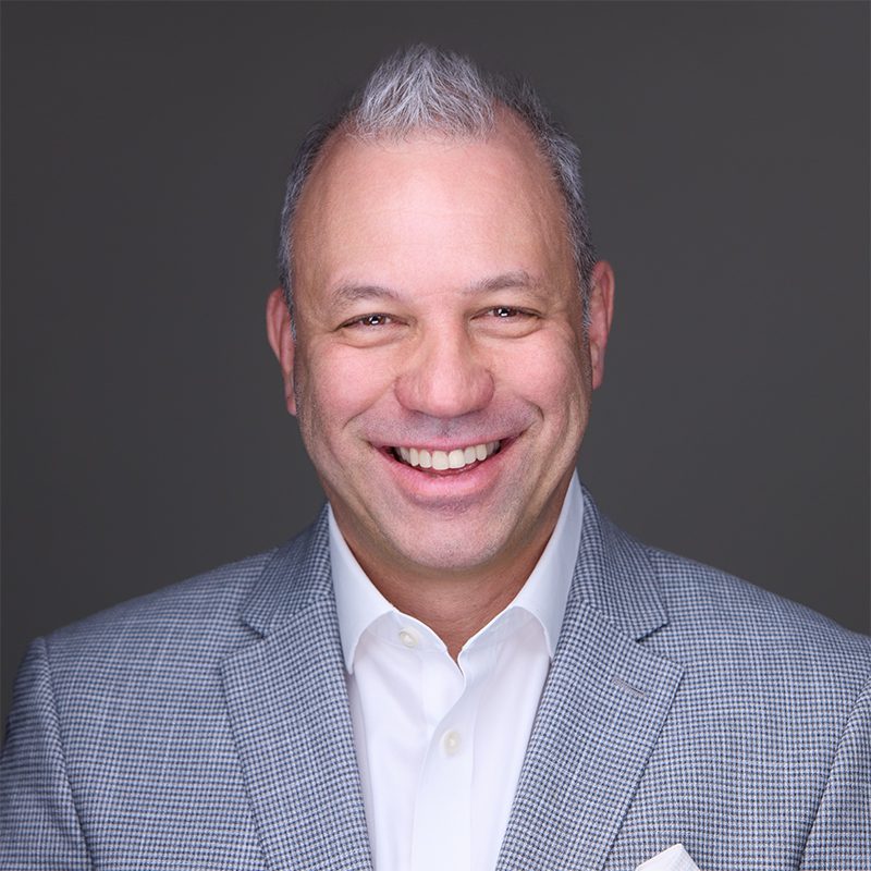 Adam Levin smiling, wearing a light houndstooth blazer